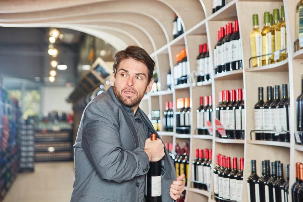 Uomo intento a rubare una bottiglia di vino in un supermercato, nascondendola sotto la giacca